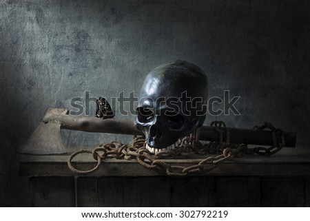 Still life photography with human skull, butterfly, rusty chains and old axe on wood table