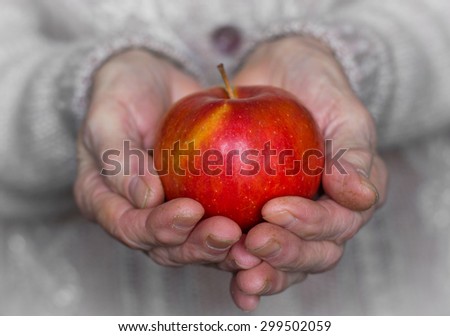 red apple in warm wrinkled grandmother\'s hands