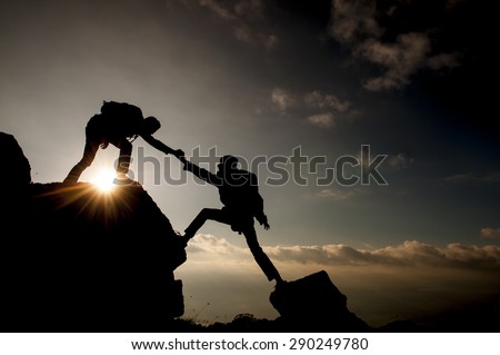 Couple hiking help each other silhouette in mountains