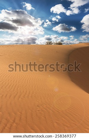 Red sand dune, blue sky , sun and clouds
