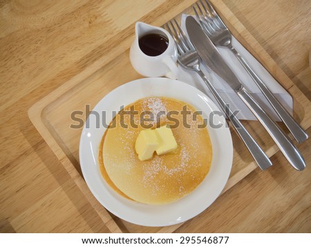 Pancakes on a white dish  with a small jug of syrup, serve on the wooden plate