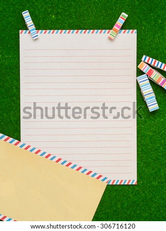 A letter paper with yellow envelop and colorful clips on green background
