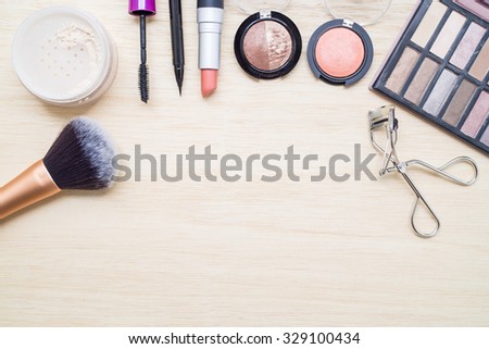 Woman earth tone cosmetics - eyeshadow, brush on, lipstick, eye liner, mascara, powder, brush, eyelash curler. Top view with space for text.
