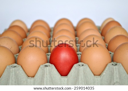 Red Easter egg among brown eggs in egg box