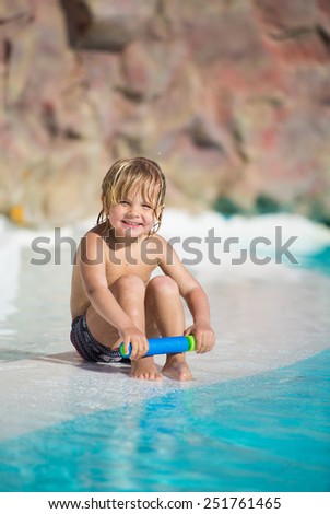 Happy little boy playing with water toy in the swimming pool