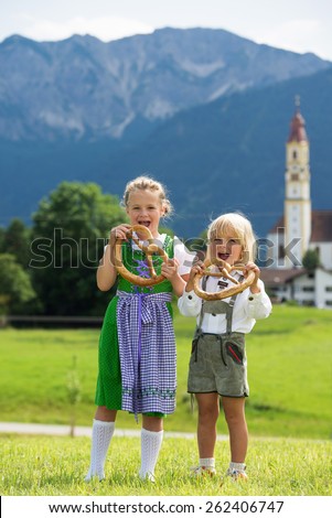 Two little children in traditional German bavarian clothes hold pretzel in the hands
