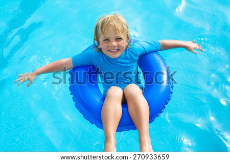 Happy little boy  with blue life ring has fun in the swimming pool