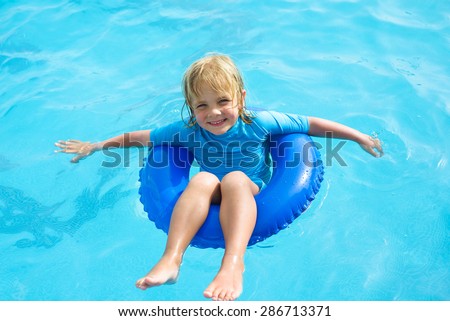 Smiling little boy with blue life ring has fun in the swimming pool