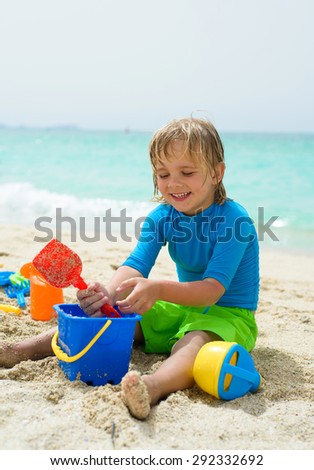 Smiling little boy plays in the sand at the beach