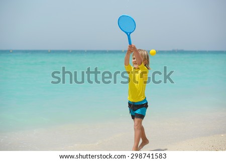 Little boy plays beach tennis on summer vacation