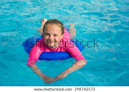 Pretty little girl  with blue life ring has fun in the swimming pool