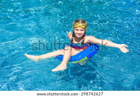 Smiling little girl  with blue life ring has fun in the swimming pool