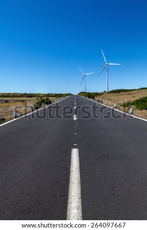 a straight road with two wind turbines over the area with a blue sky