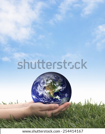 Earth Day. Hands holding earth over grass on a blue sky. The planet earth image provided by NASA.