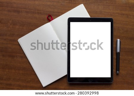 Still-life of work desk with tablet, notebook and pen.\
\
White screen on device is easy to select and place your own website presentation page and show how amazing is looks.
