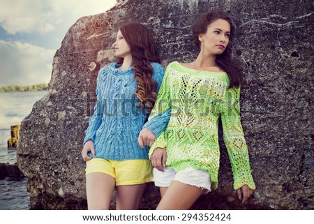Two women in knitted sweaters, pose at the rock at the sea