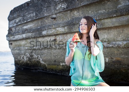The woman costs in water, listens to music and eats a water-melon