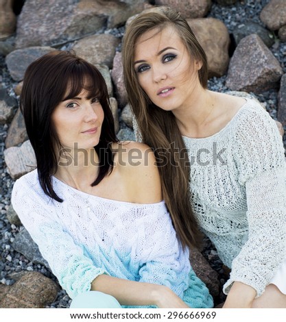 Two women in knitted sweaters, pose at the rock at the sea