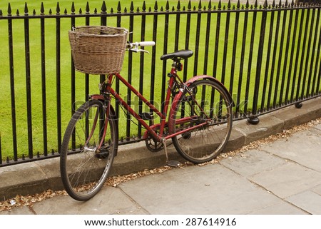 Red bicycle with a basket and white handle by black metal fence.