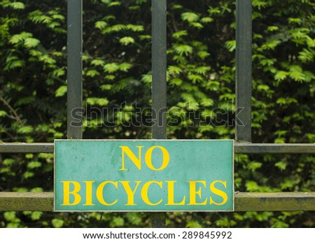 Yellow inscription No Bicycles on teal Sign on black fence and green background