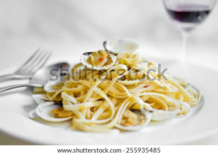 Delicious seafood pasta dish, clam linguine, served with red wine on a white plate with a white background and silver fork and spoon cutlery.