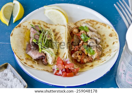 Cooked tortillas, one is rare beef, sour cream, guacamole and shallots, the other is chicken and chili peppers, both served with salsa, lemon and salt.