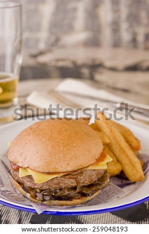 Sloppy Joe beef burger with cheese and onions served with extra chunky thick chips. Glass of beer in the background to the left and cutlery to the right.