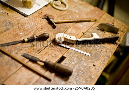 Wood working tools and the neck of a new violin rest on a bench in a Luther\'s studio. Hammer, chisel, measuring stick and a plane.