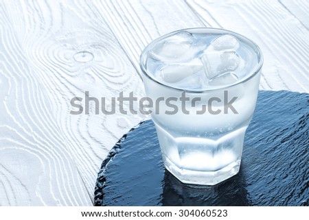 a glass of water with ice cubes   on black stone tray at white colored wooden table