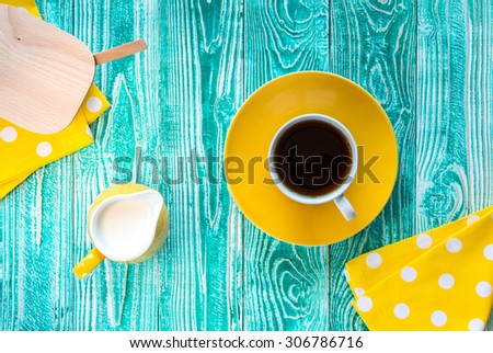 cup of black tea on yellow plate and yellow milk jug and sugar-bowl\
\
on turquoise colored old wooden table with yellow napkin at polka dots top view