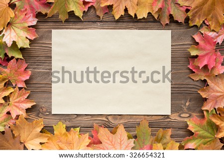 a sheet of craft paper a sheet of paper, surrounded by leaves  fallen leaves on wooden background, top view, copy space. free space for text