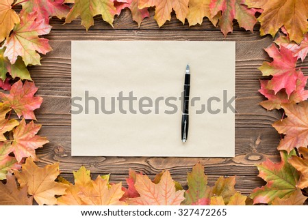 a sheet of craft paper and pen with fallen leaves on wooden background, top view, copy space. free space for text