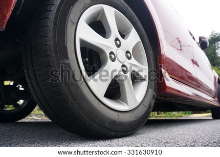 Close up of a black car tyre park on the road. Side view of Red car. View from bottom of the car.