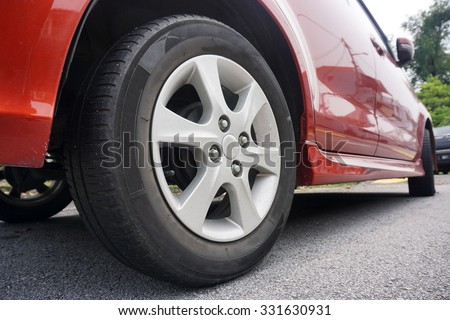 Close up of a black car tyre park on the road. Red car with tyre