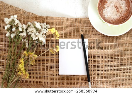 empty paper note, black pencil and cocoa on white wooden and gunny sack background  with white and yellow flowers