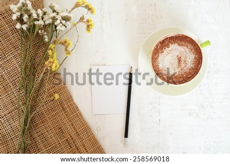 empty paper note, black pencil and cocoa on white wooden and gunny sack background  with white and yellow flowers