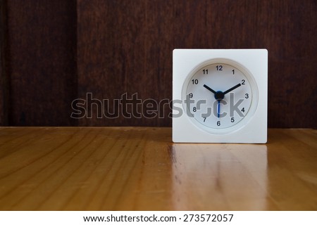 The white alarm clock on dark wooden background.