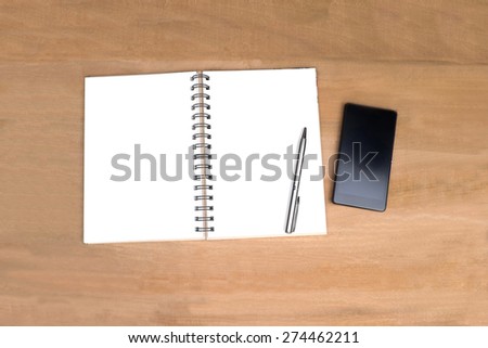 Empty open note book and mobilephone on wooden office table background.View from above with copy space.