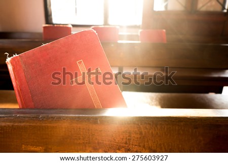 The old red books or red worship songbooks at wooden  bench in church  with soft sun light. Vintage Style.