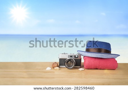 Idea concept. Red pink tower, blue hat, old vintage camera and shells over wooden table on sunshine blue sky and ocean background.
