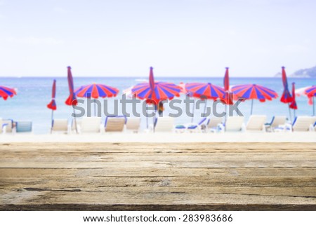 Travel idea concept. Wooden desk or wooden floor on sand beach side with beach chairs and colorful umbrella