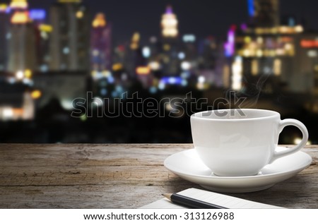 Wood floor and a cup of hot coffee with blurred abstract background of city night lights downtown city view : Wooden table with blur background of cityscape