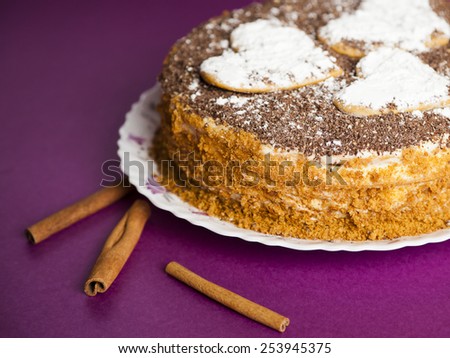 cake with chocolate crumb. Honey cake. Cake hearts. Cake on violet background. Cake with sticks cinnamon. Cinnamon sticks. Cake on white plate. Baked cake. White powder cake. Bake food. Baking