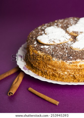 cake with chocolate crumb. Honey cake. Cake hearts. Cake on violet background. Cake with sticks cinnamon. Cinnamon sticks. Cake on white plate. Baked cake. White powder cake. Baking food