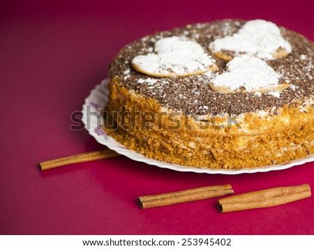 cake with chocolate crumb. Honey cake. Cake hearts. Cake on red background. Cake with sticks cinnamon. Cinnamon sticks. Cake on white plate. Baked cake. White powder cake. Bake food. Baking