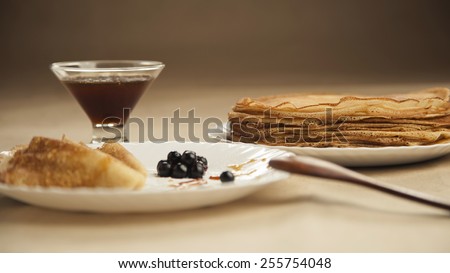 Russian pancakes with wooden spoon and honey on table. Russian cuisine. Taste pancake. Black currant on white plate with pancakes. Blini. Maslenitsa. Pancake week. Butter Week. Cheesefare Week. Baking