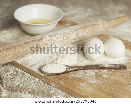 Preparations for homemade baking. Basic ingredients for baking. Kitchen utensil with eggs rolling-pin wood spoon meal. Meal on table with cutting board. Flour. Baking