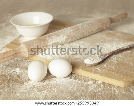 Preparations for homemade baking. Basic ingredients for baking. Kitchen utensil with eggs rolling-pin wood spoon meal. Meal on table with cutting board. Flour