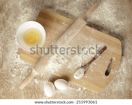 Preparations for homemade baking. Basic ingredients for baking. Kitchen utensil with eggs rolling-pin wood spoon meal. Meal on table with cutting board. Flour