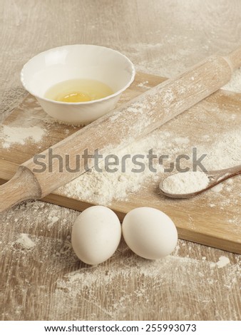 Preparations for homemade baking. Basic ingredients for baking. Kitchen utensil with eggs rolling-pin wood spoon meal. Meal on table with cutting board. Flour. Baking